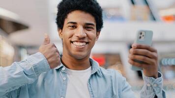 Portrait satisfied happy african guy man with phone smartphone modern gadget looking at camera shows like thumbs up recommends wifi cellular connection 5g mobile app promotion website good network photo