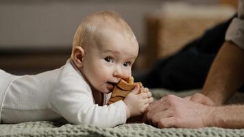 Caucasian family unrecognizable father daddy play with little daughter son infant newborn toddler lying at home on floor with toys baby bites wooden constructor teething concept, man stroking head photo