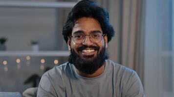 Smiling adult 30s indian arabian bearded man vlogger looking at camera talk make live conference call online chat streaming recording blog vlog at home distant conversation close up webcam view photo
