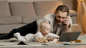 Caucasian multitasking father working from home with laptop quarantine with little baby infant newborn lying on floor talking phone solve business problems. Exhausted parent with hyperactive child photo