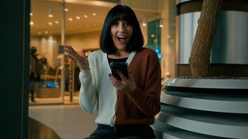 Woman indoors with phone shocked reaction female girl win with mobile phone bet winning with cellphone wonder wow with smartphone good news looking at camera with shock pointing finger on cell screen photo