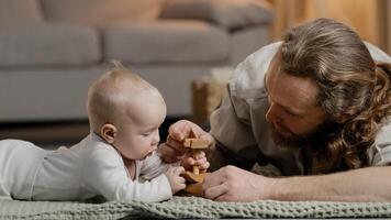 Caucasian family bearded father daddy dad with little daughter son baby infant newborn toddler playing at home on floor with toys collecting wooden constructor spend time together parenting concept photo