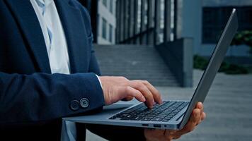 Close up male hands unrecognizable businessman typing laptop outdoors in downtown standing in city unknown entrepreneur employer man worker manager architect working with computer online app outside photo