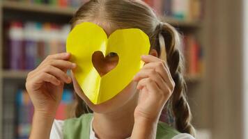 Funny happy little girl kid child schoolgirl student pupil teen daughter learner looking camera hold paper love frame symbol art class lesson education loving affectionate sign study learn in school photo