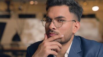 Pensive guy Arabian Indian business man thinking looking at camera close up male thoughtful puzzled businessman office think question idea solution problem search choose decide consider ponder serious photo