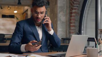 Stressed multitasking businessman Indian Arabian male guy annoyed employer manager consultant talking mobile phone shout working laptop writing documents anxious business man problem overwork office photo