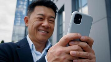 Close up bottom view happy positive smiling formal Asian middle-aged businessman adult 40s worker man employer entrepreneur chatting in mobile phone browsing texting in smartphone outdoors in city photo