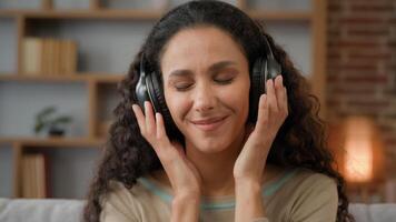 Front view close up smiling Hispanic woman with smiling enjoining lady relaxing at home with closed eyes listening to music in headphones audio sound song feeling well good mood hobby holiday indoors photo
