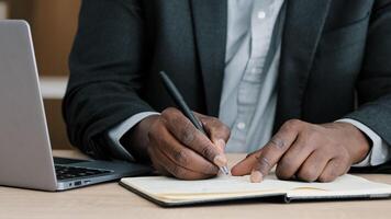 Close-up male hands writing in notebook with pen make notes information financial analysis startup project management idea sitting at desk in office using laptop unrecognizable middle-aged businessman photo