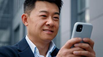 Happy male in city outdoors looking phone screen Asian 40s businessman entrepreneur employer man using mobile app map navigation in smartphone chatting browsing working distant virtual organizer photo