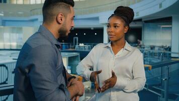 Diverse colleagues multiethnic multiracial coworkers talking in company office. African American woman businesswoman and Arabian Indian man businessman talk speak conversation discuss in business hall photo