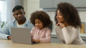 African American family at kitchen shopping online together mother father teach child daughter little girl at home kitchen using laptop food delivery kid computer playing e-learning parental control photo