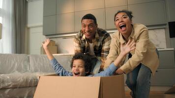 Happy African American family celebrate relocation new home joyful mother father run push cardboard box with little child boy kid ride inside cheerful parents son playing fun moving day loan mortgage photo