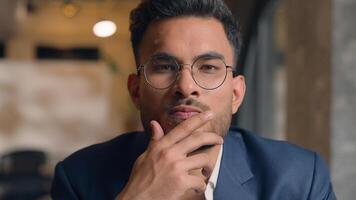 Pensive guy Arabian Indian business man thinking looking at camera close up male thoughtful puzzled businessman office think question idea solution problem search choose decide consider ponder serious photo