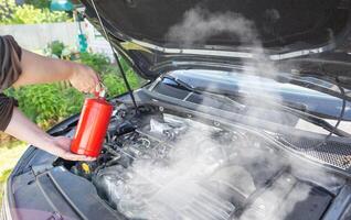 The driver of the car directs a powder fire extinguisher at the engine compartment of the car in which there is fire and smoke. Car fire, background. Electrical short circuit photo