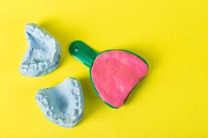 Dental spoon with alginate plastic mass for taking an impression of the dental jaw on a yellow background. Blue plaster dental jaw on a yellow background. Orthodontics in dentistry photo