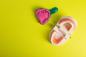 Green dental spoon for taking a dental impression in a mock-up of a dental jaw on a yellow background. Making an artificial jaw for malocclusion. Manufacturing of dental prostheses photo