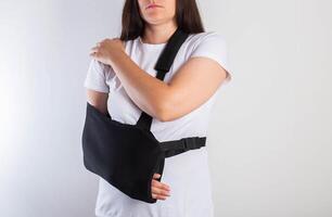 A girl on a white background with a black supporting medical bandage after a dislocation of the shoulder joint and a bone fracture. Rehabilitation after injury, orthopedics and traumatology photo