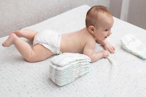 The legs of a baby in a diaper against the background of a stack of children's comfortable diapers, close-up. Copy space for text photo