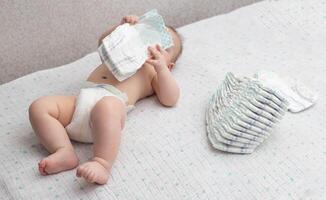 A little caucasian baby boy in a diaper lies on a white background and plays with a bunch of diapers. Copy space for text photo