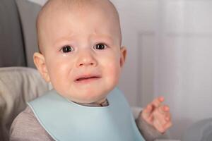 A little boy at the age of 8 months is crying and looking at the camera. Pain and discomfort during teething in infants. Copy space for text photo