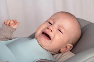 A small baby 6 months old is crying and looking at the camera. The concept of bloating and pain in the abdomen in children, colic. Copy space for text photo
