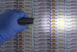 An expert checks American money dollars for counterfeiting with an ultraviolet flashlight. The concept of detention and counterfeiting, copy space for text photo