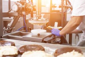 The pastry chef makes cake using modern equipment for the production of cakes. Line for spreading cream on cake, biscuit photo