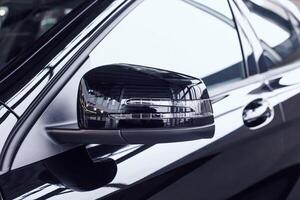 Modern beautiful side rear-view mirror in a new car with a built-in direction indicator. Black car at a car dealership, aerodynamic photo