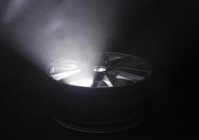 Modern beautiful car alloy wheel in the form of rays that is highlighted by rays of light and sparkle, black background photo
