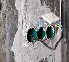 An electric switch hangs on wires from socket boxes built into a concrete wall. The danger of electricity photo