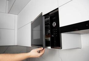 A man opens the door of a microwave oven in which there is a grilled chicken in a plate. The concept of grilling and convection in a microwave. photo