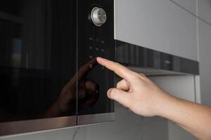 A man presses his finger on the touch panel of a microwave oven to turn on the defrost function. High tech modern microwave oven photo