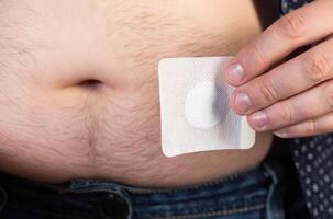 A modern medical patch for prostatitis and urinary tract infections. A man glues a urological patch on his stomach, close-up photo
