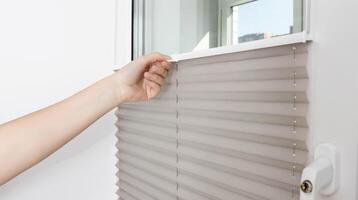 A man opens the blinds on the window to let sunlight into the room. Aluminum classic blinds with scaffold fixing system. Close-up photo