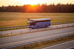 A blue comfortable bus transports passengers along the highway in the evening against the backdrop of sunset. Concept of traveling to another country by bus from a travel agency, convenience photo