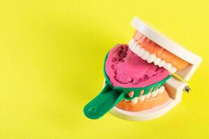 Green dental spoon for taking a dental impression in a mock-up of a dental jaw on a yellow background. Making an artificial jaw for malocclusion. Manufacturing of dental prostheses photo