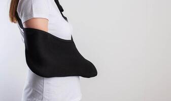 A girl in white with a fixing black bandage on her arm after an injury, a fracture of the radius and a sprain. Arm support bandage, hand immobilization. Copy space for text photo