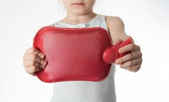 The girl holds a red heating pad with warm water in her hands at outstretched arms. Concept for heat treatment of muscle spasms and pain, close-up photo