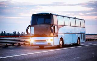 A blue comfortable bus carries passengers along the highway in the evening with the headlights on. The concept of travel and tourist tours from travel agencies. photo