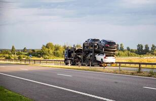 Delivery of cars on a cargo transporter along the highway in the summer. Business in the delivery and sale of cars, industry photo