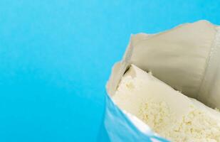 Powdered baby food for preparing milk formula in a shiny bag on a blue background, copy space for text photo