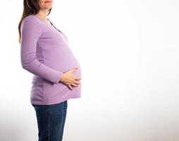 A pregnant girl in a purple jacket holds her stomach on a white background. Concept of determining the gender of a child, the birth of a future baby, boy or girl. Copy space for text photo