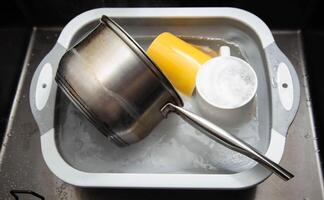 Dirty dishes in a sink basin with hot water and foam from an environmental oxygen cleaner. A modern product for removing dirt and stains. photo