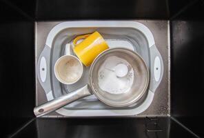 measuring spoon with granules of environmentally friendly oxygen bleach in a basin with dirty dishes. Cleaning grease and dirt from dishes, close-up photo
