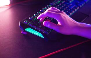 Gamer plays game on PC at computer club, keyboard mouse RGB lightning animation close up. photo