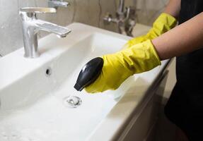 A girl washes and cleans the sink with a cleaning agent wearing yellow rubber gloves. Whitening and shine product, close-up. Copy space for text photo