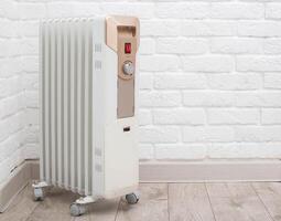 Electric heating radiator with temperature control on the background of a white brick wall. The concept of heating a room without turning on the heating in the apartment. The cold season is autumn photo