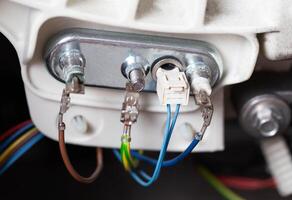 An electric heating element with a thermostat is connected with electrical chips. Repair and replacement of temperature sensor and heating element, hard water, close-up photo