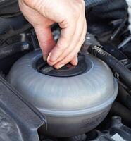 A man unscrews the expansion tank cap of a car with coolant, close-up. Engine overheating problem, airlock photo